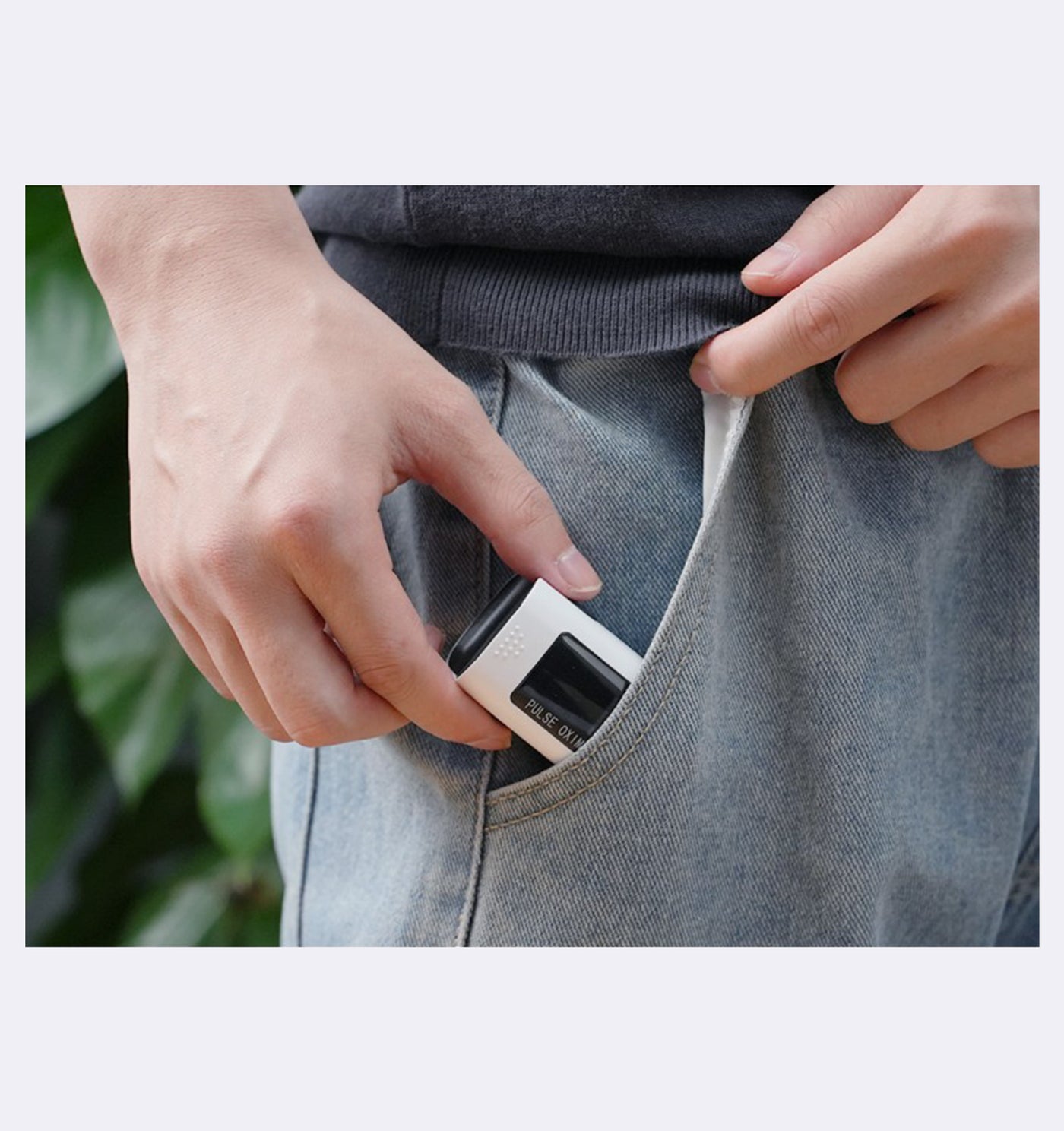 Person inserting a small black and white device into their pocket with a blurred green plant background