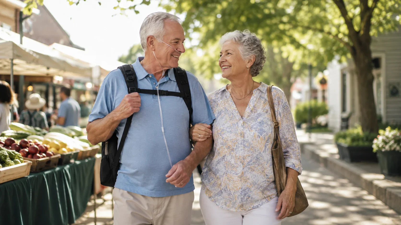 Older man wearing a nasal cannula and carrying a lightweight portable oxygen concentrator while walking through a farmers market with his wife.