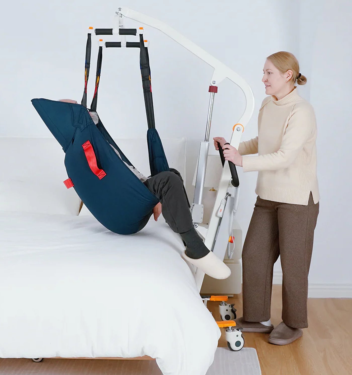 Person using a medical lift to assist another person onto a bed.